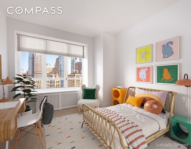 bedroom featuring a city view, radiator heating unit, and wood finished floors