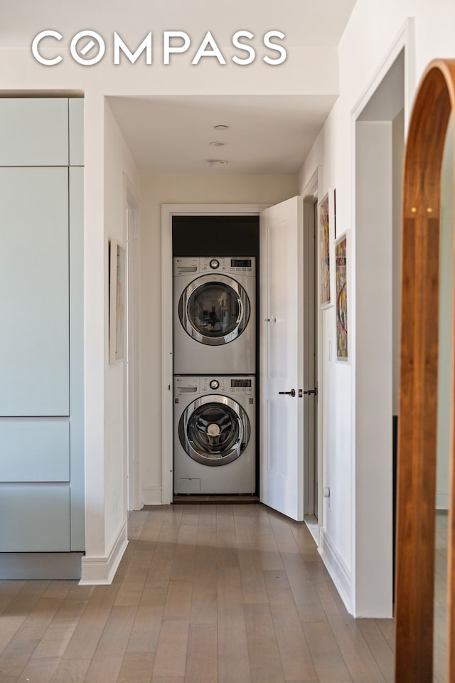 washroom with laundry area, stacked washer / dryer, wood finished floors, and baseboards