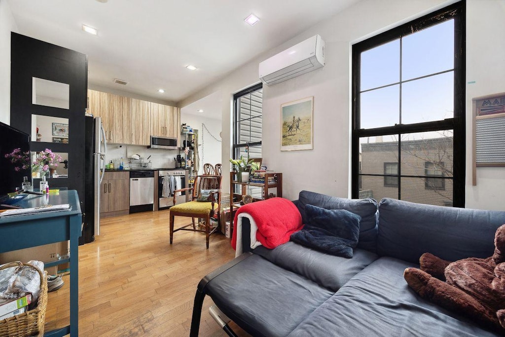 living room featuring visible vents, recessed lighting, an AC wall unit, and light wood-type flooring