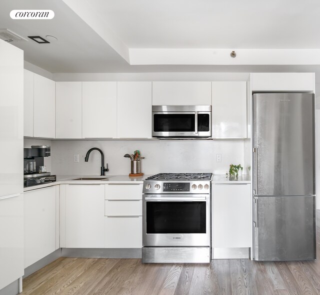 kitchen featuring appliances with stainless steel finishes, a sink, light countertops, light wood-style floors, and white cabinetry