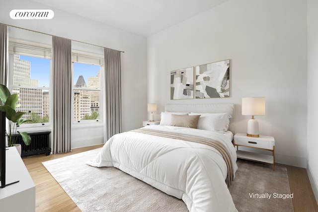 bedroom featuring wood finished floors, visible vents, baseboards, radiator heating unit, and a view of city