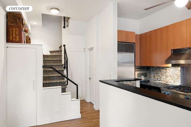 145 Nassau St Unit 8A, New York City, NY 10038 - kitchen featuring under cabinet range hood, appliances with stainless steel finishes, decorative backsplash, light wood-style flooring, and brown cabinetry