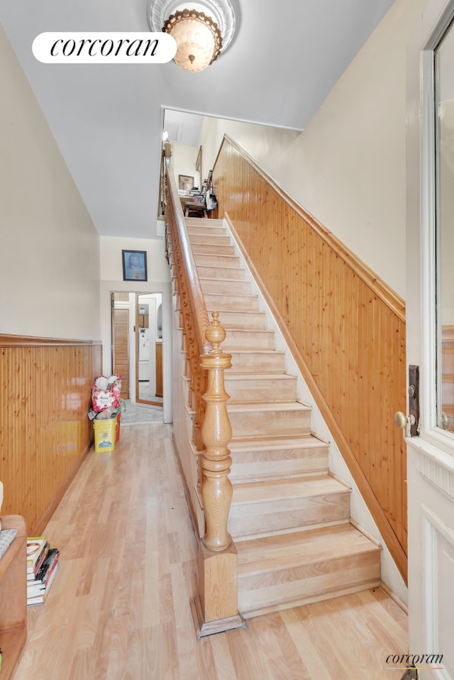 stairway featuring wood finished floors, a wainscoted wall, and wood walls