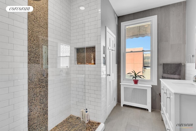 full bathroom featuring a tile shower, radiator, vanity, and tile walls