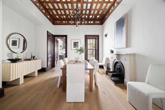 dining room featuring a chandelier, a fireplace with raised hearth, coffered ceiling, and wood finished floors