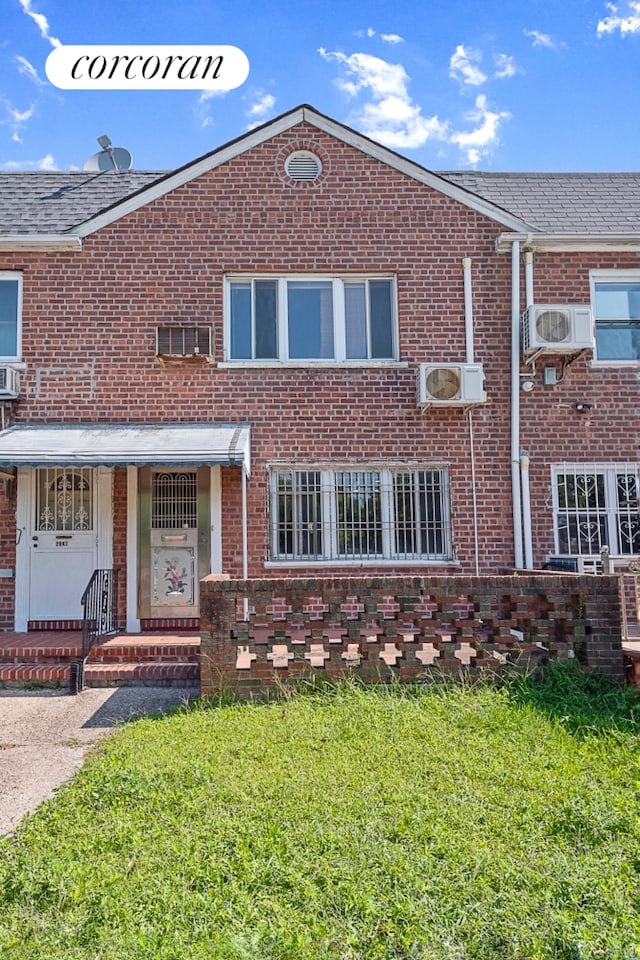 multi unit property featuring a wall mounted air conditioner, an AC wall unit, a front lawn, a shingled roof, and brick siding