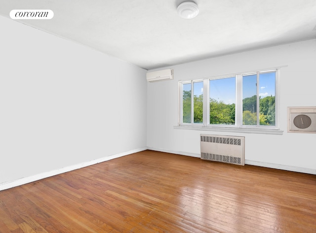 empty room with an AC wall unit, hardwood / wood-style floors, radiator, baseboards, and visible vents