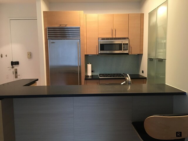 kitchen featuring a breakfast bar area, a peninsula, appliances with stainless steel finishes, decorative backsplash, and dark countertops