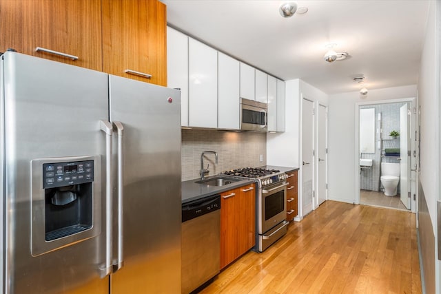 kitchen featuring light wood finished floors, a sink, stainless steel appliances, white cabinetry, and tasteful backsplash