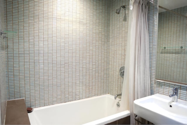 bathroom with tile walls, tiled shower / bath combo, and a sink