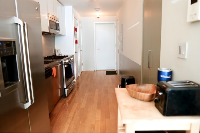 kitchen with light wood finished floors, backsplash, appliances with stainless steel finishes, white cabinetry, and modern cabinets