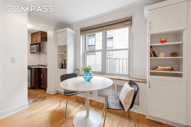 dining room featuring light wood finished floors, built in shelves, and baseboards