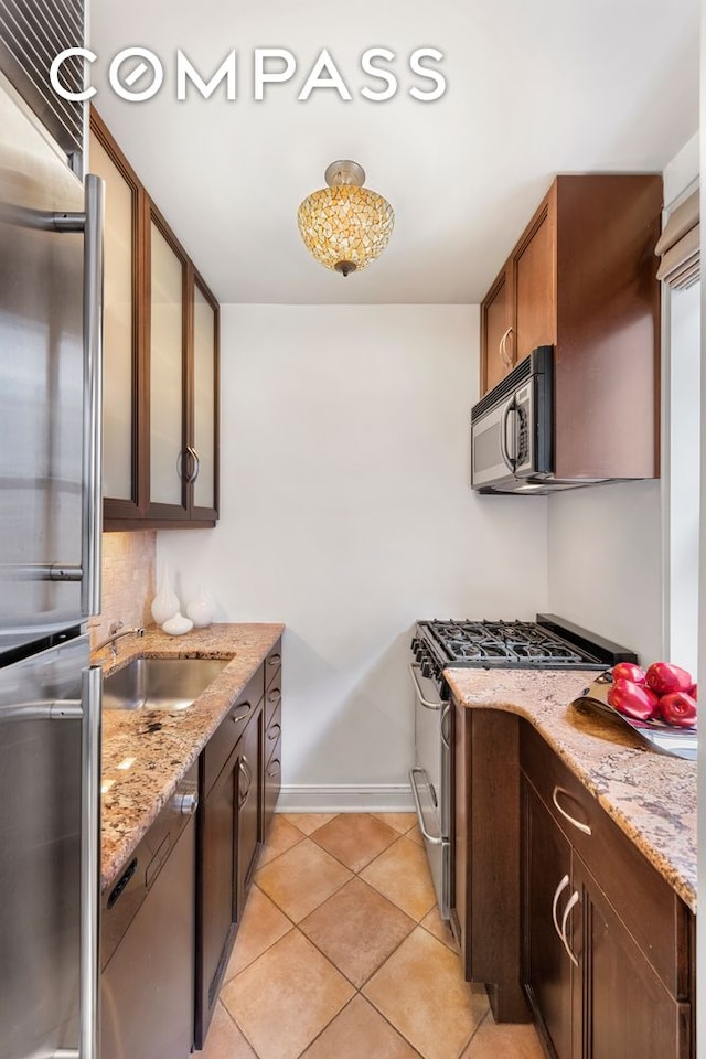 kitchen with light tile patterned floors, tasteful backsplash, glass insert cabinets, appliances with stainless steel finishes, and light stone countertops