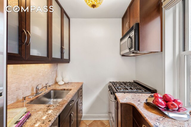 kitchen with dark brown cabinetry, a sink, appliances with stainless steel finishes, backsplash, and glass insert cabinets