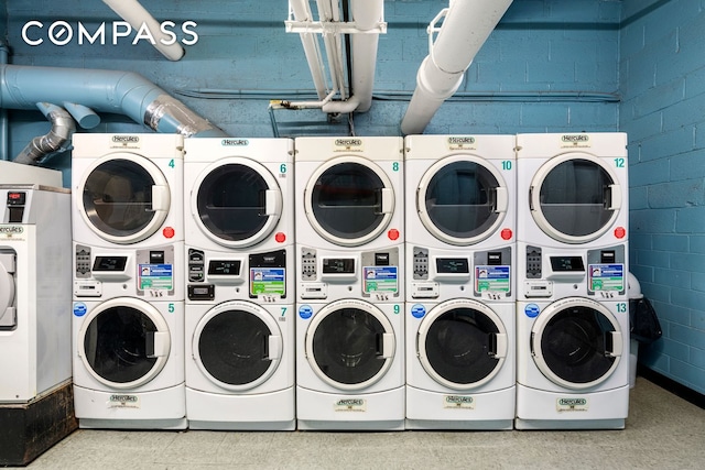 shared laundry area featuring stacked washer / dryer, washing machine and dryer, and concrete block wall