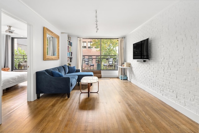 living room featuring brick wall, wood finished floors, baseboards, ornamental molding, and rail lighting