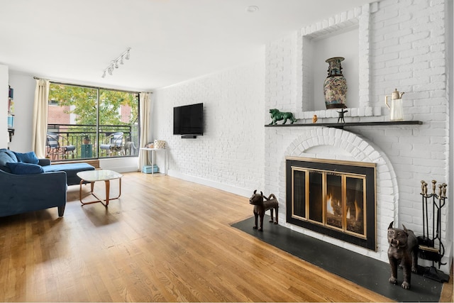 living room featuring brick wall, a fireplace, wood finished floors, baseboards, and rail lighting