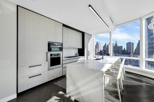 kitchen with light stone counters, a sink, a view of city, a kitchen breakfast bar, and modern cabinets