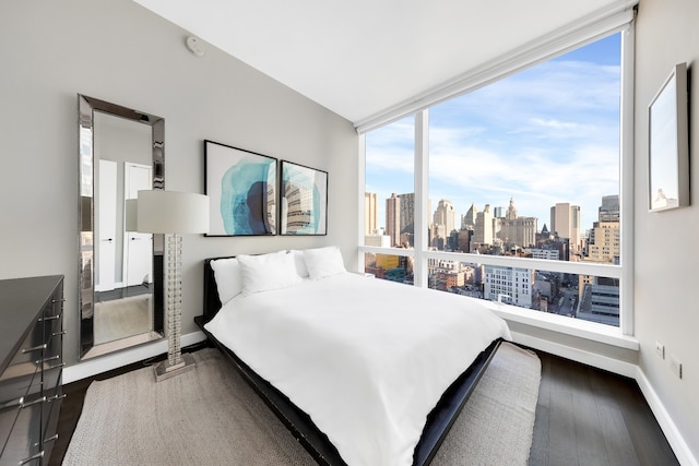 bedroom with a view of city, dark wood finished floors, and baseboards