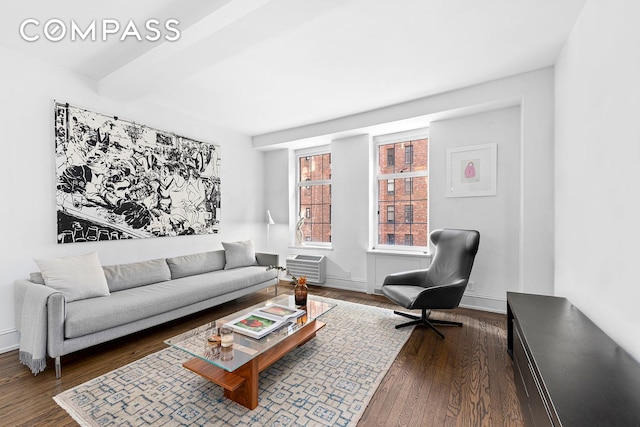 living area with a wall unit AC, baseboards, dark wood-type flooring, and beamed ceiling