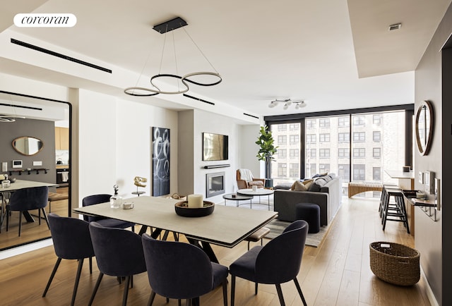 dining area featuring visible vents, a glass covered fireplace, light wood-style flooring, floor to ceiling windows, and track lighting