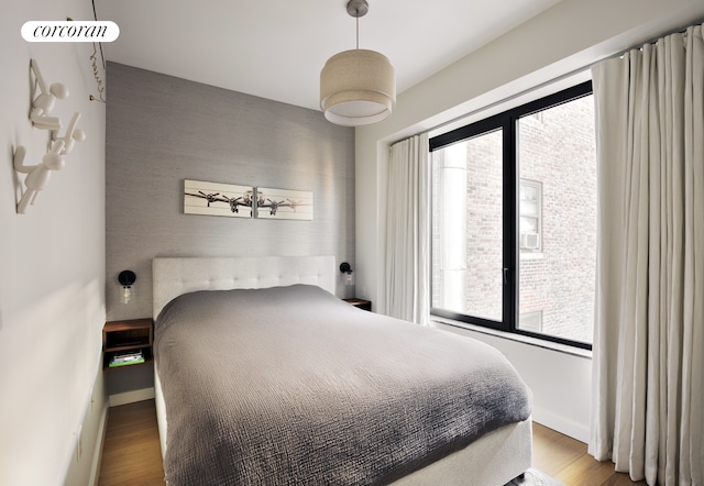 bedroom featuring baseboards, multiple windows, an accent wall, and wood finished floors