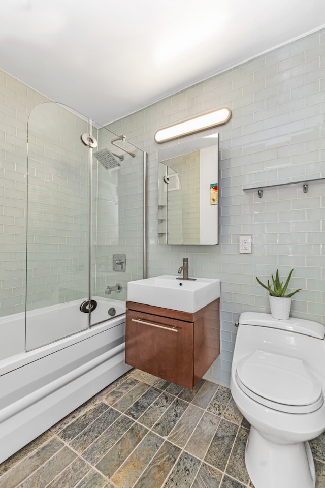 bathroom with toilet, combined bath / shower with glass door, tile walls, and vanity