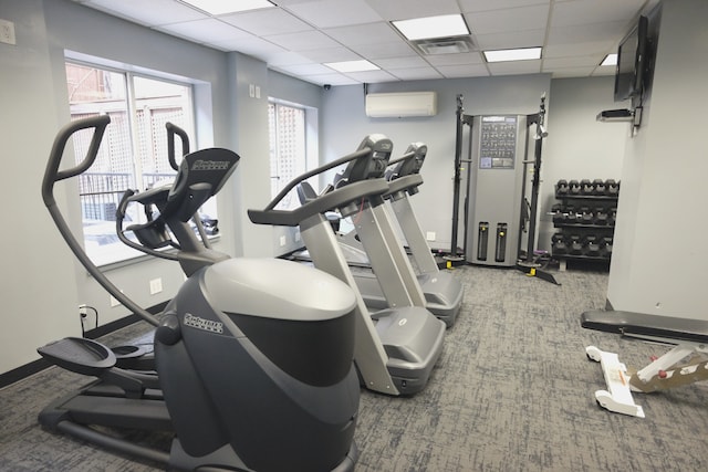 gym featuring a paneled ceiling, a wall unit AC, visible vents, and baseboards