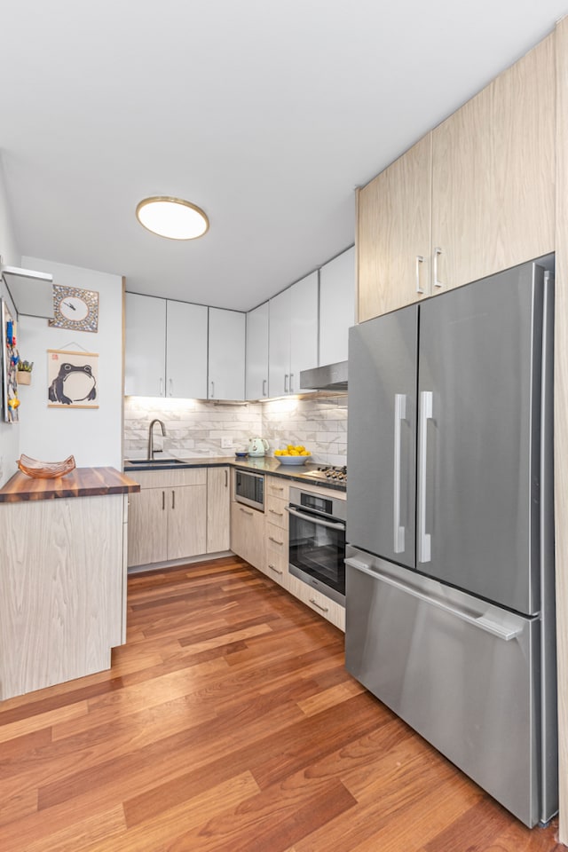 kitchen with light wood-style floors, appliances with stainless steel finishes, a sink, under cabinet range hood, and backsplash