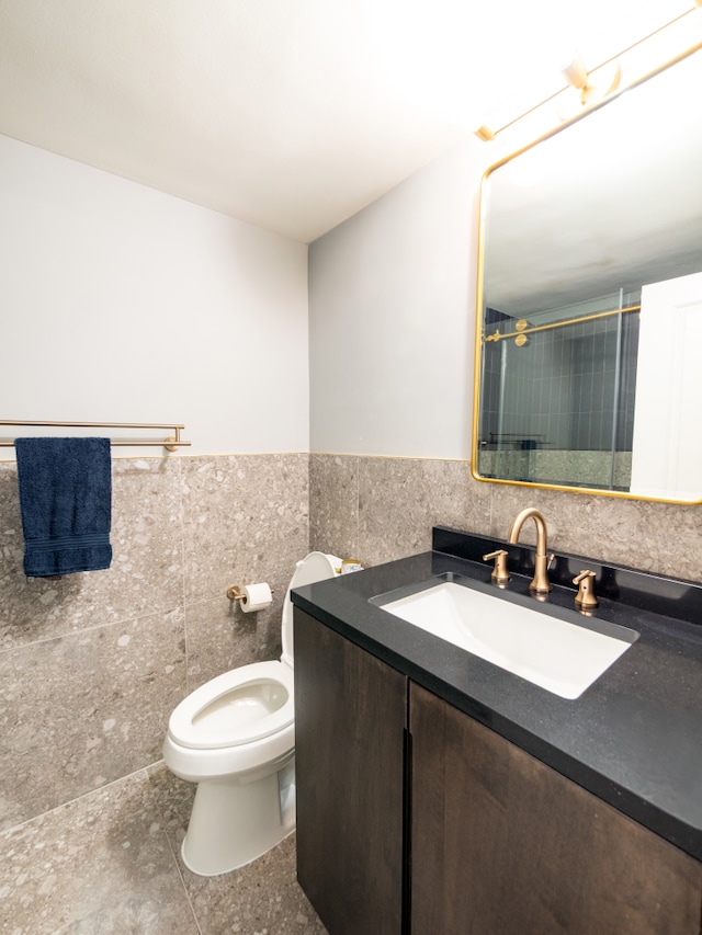 full bathroom with tile walls, walk in shower, toilet, vanity, and wainscoting