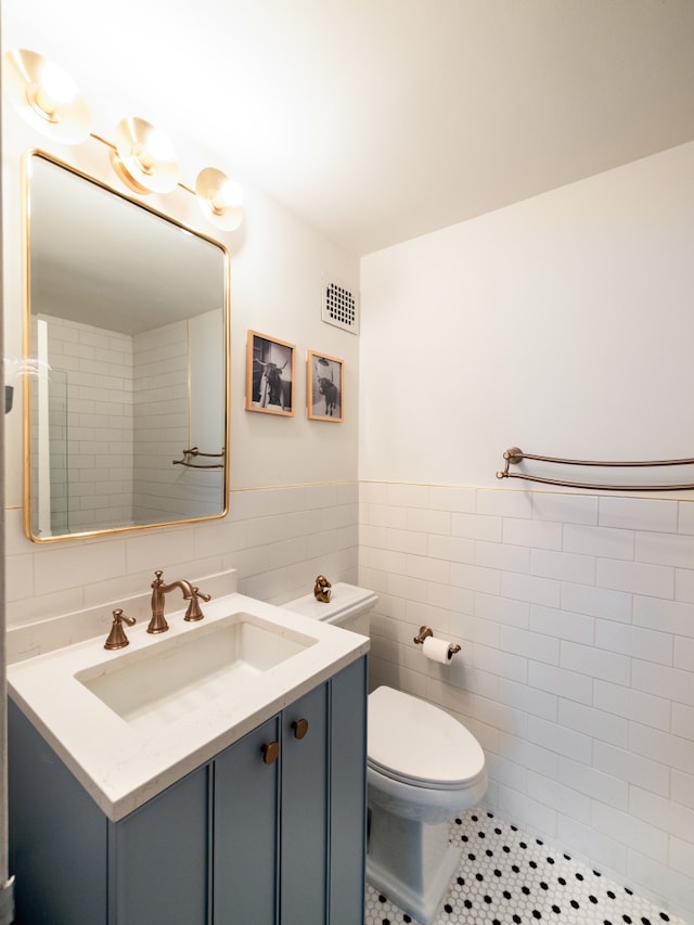 bathroom featuring vanity, tile walls, toilet, visible vents, and wainscoting