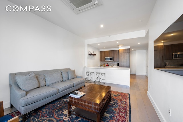 living area with light wood-style flooring, visible vents, baseboards, and recessed lighting