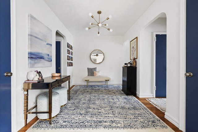 hallway with an inviting chandelier, wood finished floors, arched walkways, and baseboards