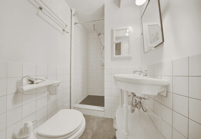 full bath with a wainscoted wall, tile walls, toilet, a tile shower, and tile patterned flooring