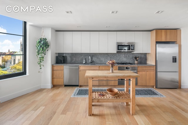 kitchen with appliances with stainless steel finishes, decorative backsplash, baseboards, and light wood-type flooring