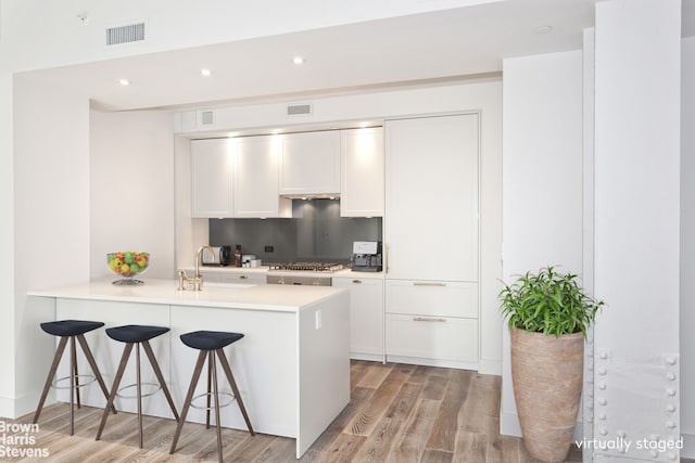 kitchen featuring a peninsula, a breakfast bar area, visible vents, and light wood-style floors