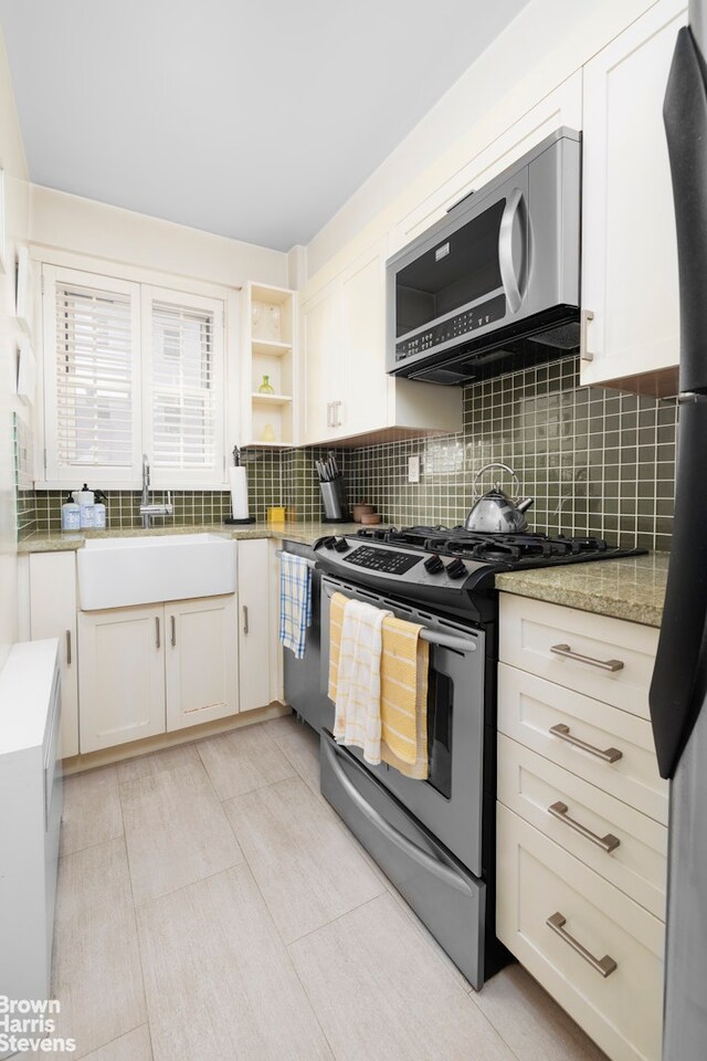 166 E 35th St Unit 10G, New York City, NY 10016 - kitchen with stainless steel range, decorative backsplash, white cabinetry, open shelves, and light stone counters