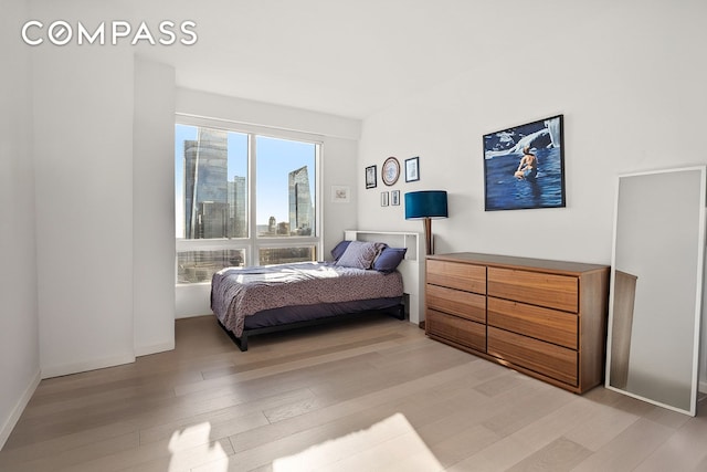 bedroom featuring baseboards, a city view, and light wood-style floors