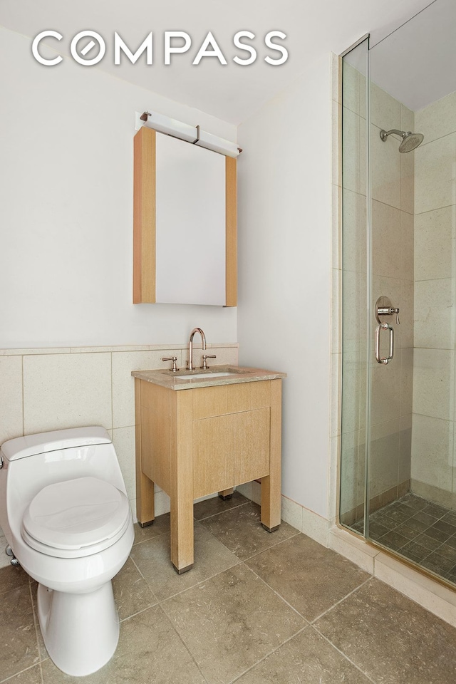 bathroom featuring toilet, a wainscoted wall, tile walls, vanity, and a stall shower