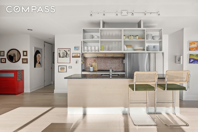 kitchen with open shelves, dark countertops, decorative backsplash, freestanding refrigerator, and a sink