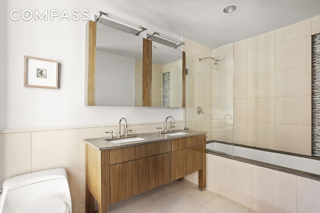 full bath featuring tiled shower / bath combo, tile patterned flooring, a sink, and tile walls