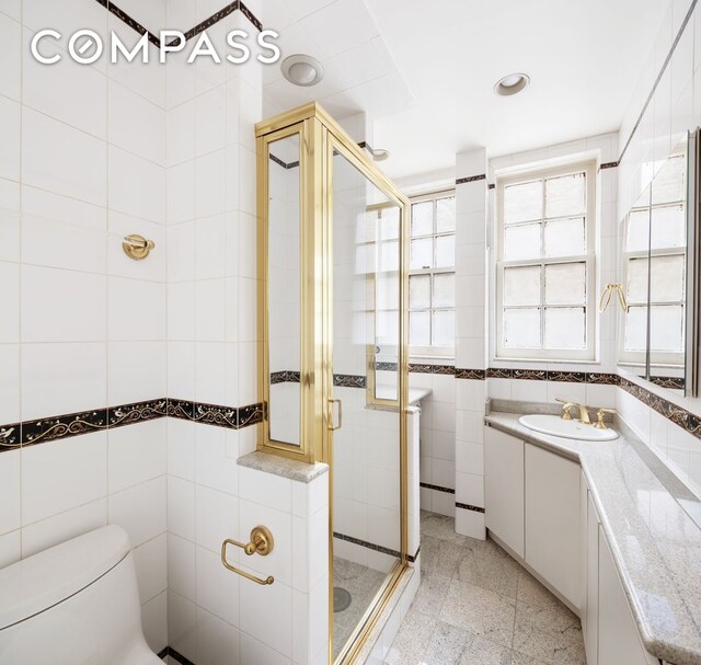 bathroom with toilet, granite finish floor, vanity, tile walls, and a shower stall