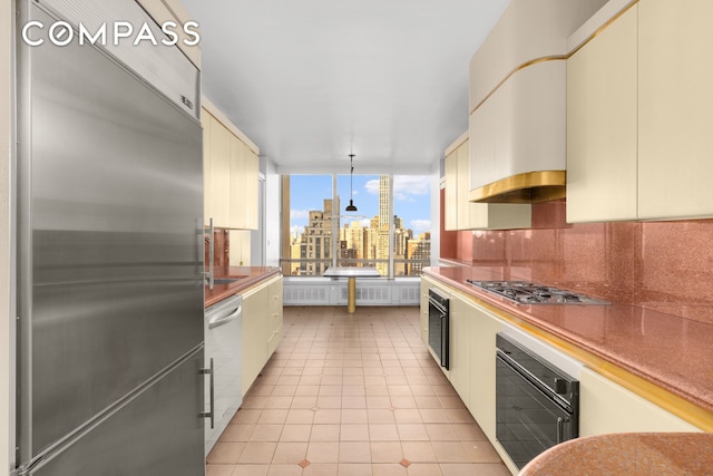 kitchen with light tile patterned floors, stainless steel appliances, cream cabinetry, decorative backsplash, and a view of city