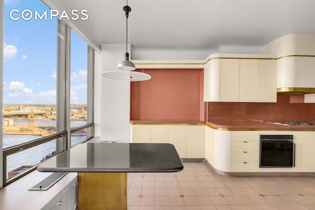 kitchen featuring black oven, hanging light fixtures, backsplash, and a water view