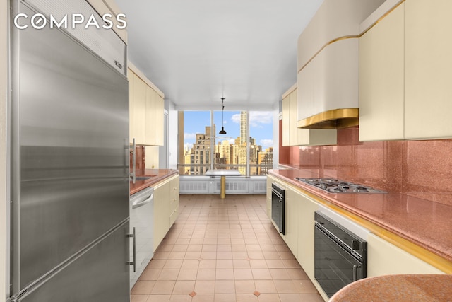 kitchen featuring a view of city, decorative backsplash, appliances with stainless steel finishes, cream cabinetry, and light tile patterned flooring