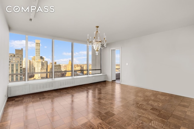 spare room with a view of city, a notable chandelier, and baseboards