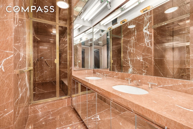 full bath with marble finish floor, a sink, a shower stall, and double vanity