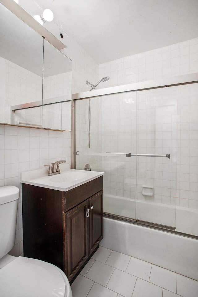 full bath featuring toilet, tile patterned flooring, combined bath / shower with glass door, vanity, and tile walls