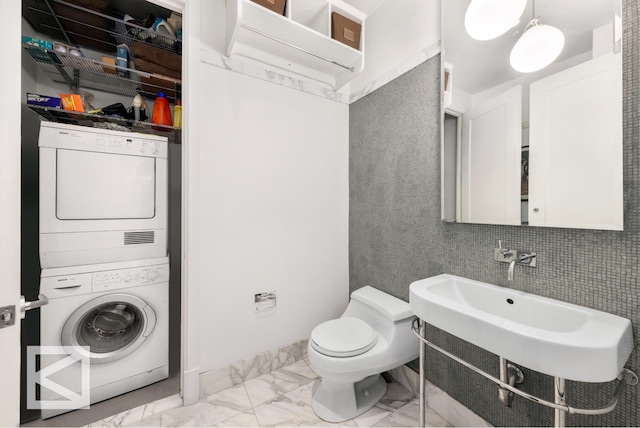 bathroom with toilet, a sink, stacked washer / dryer, and marble finish floor