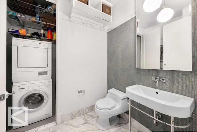 bathroom with stacked washer / dryer, marble finish floor, and toilet